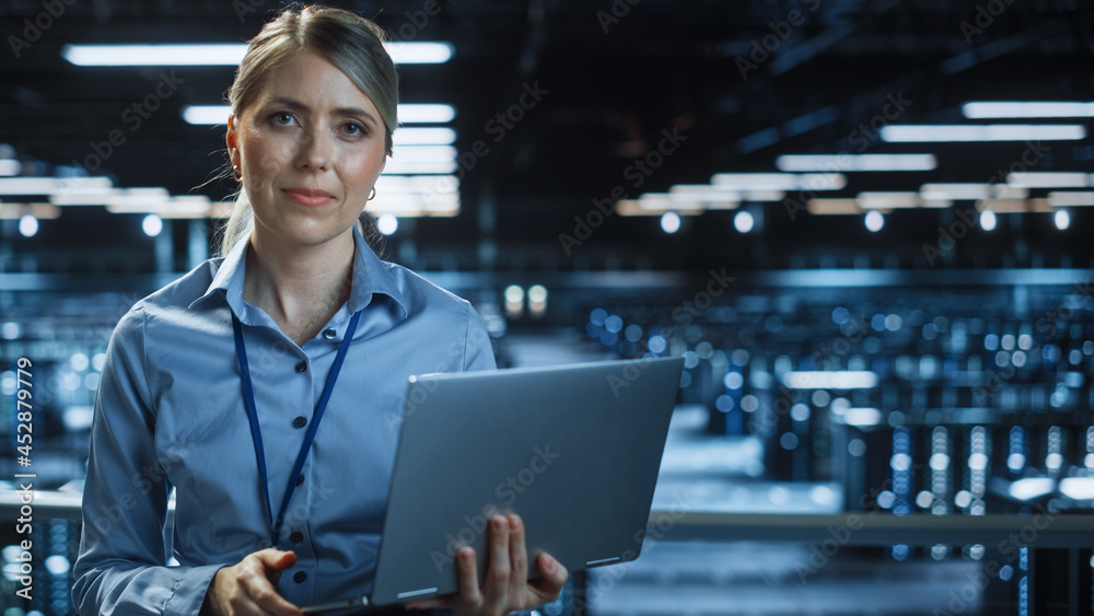 Portrait of Beautiful Smiling IT Specialist Using Laptop Computer in Data Center, Looking at Camera.