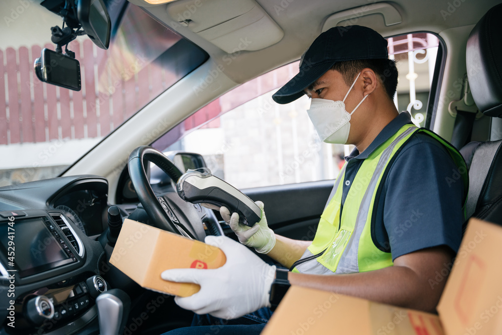 Asian delivery man using a credit card reader. In the car with parcels on the outside of the warehou