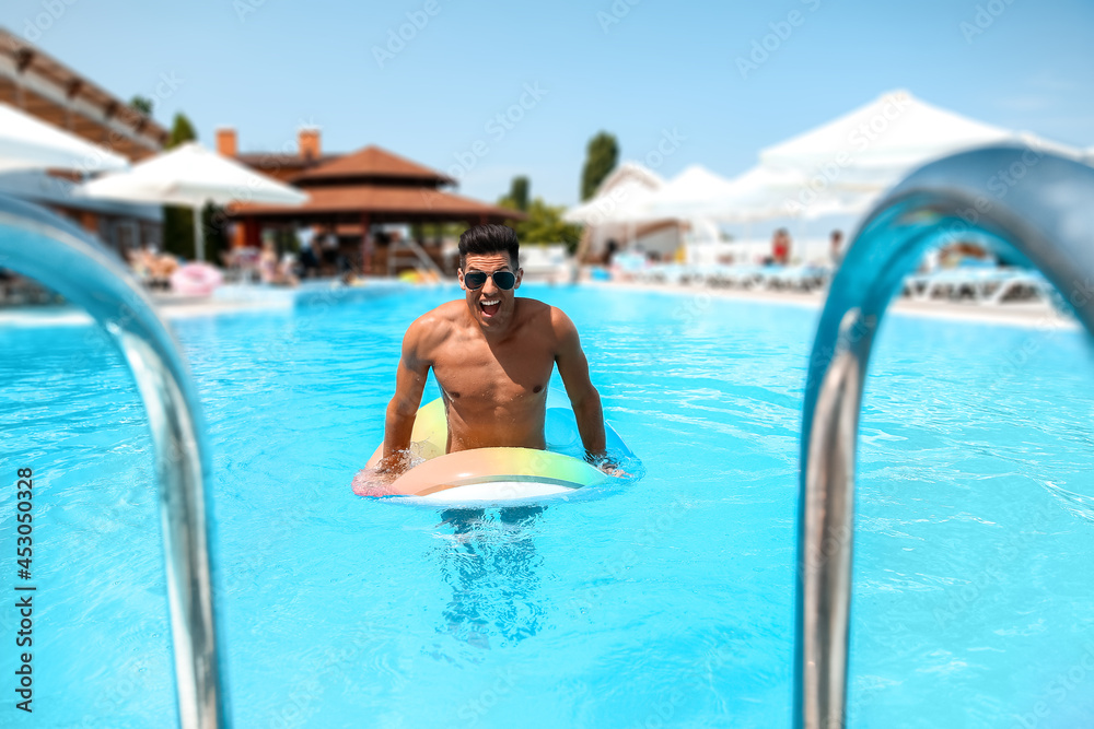 Young man with inflatable ring in swimming pool