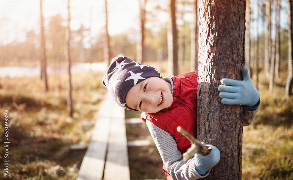 Cute boy in the forest hugging a trees trunk