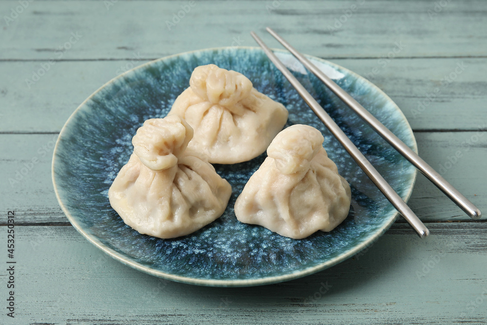 Plate with tasty dumplings and chopsticks on color wooden background, closeup