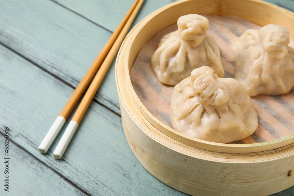 竹蒸笼，彩色木质背景，配有美味的饺子和筷子，特写