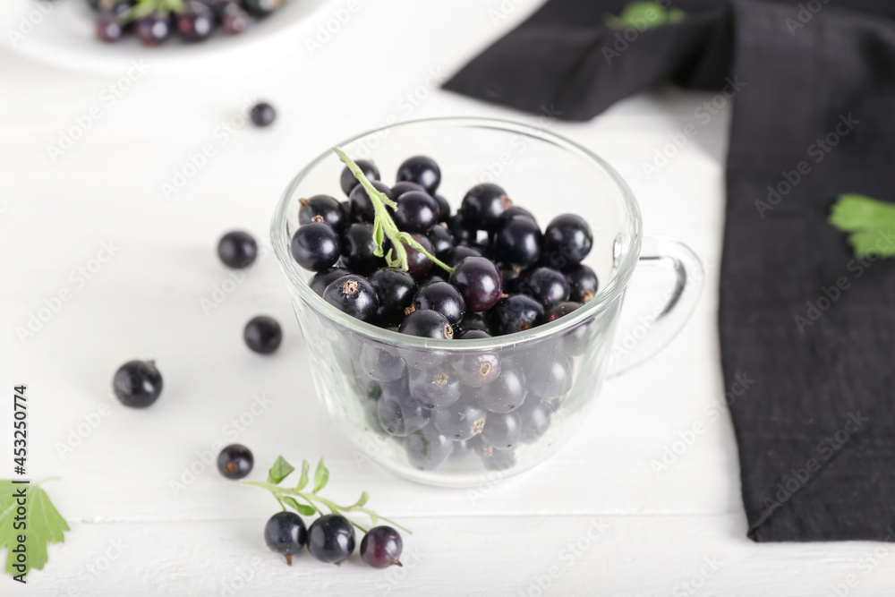 Glass cup with ripe black currant on light wooden background