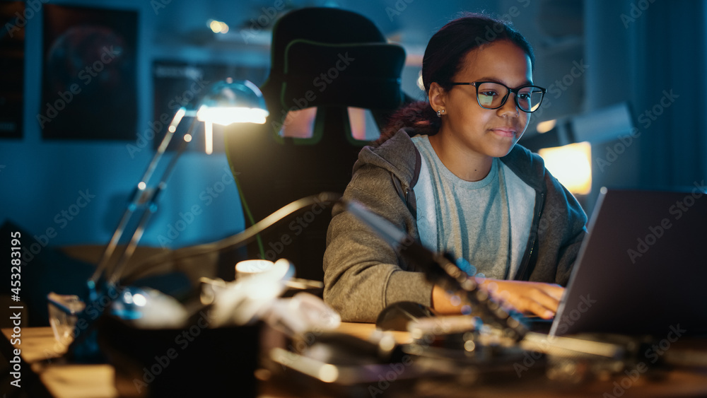 Young Teenage Multiethnic Black Girl Using Laptop Computer in a Dark Cozy Room at Home. Shes Browsi