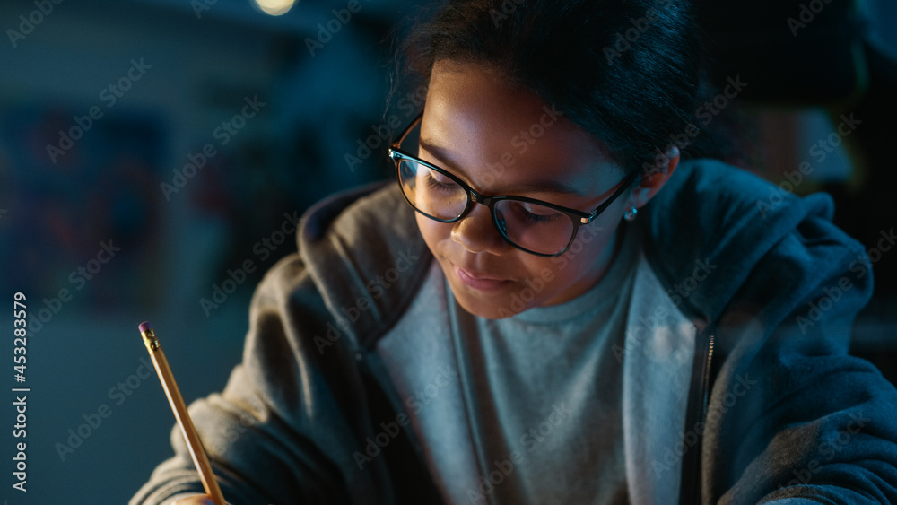 Young Teenage Multiethnic Black Girl Writing Down Homework in a Notebook with a Pencil, Using Laptop