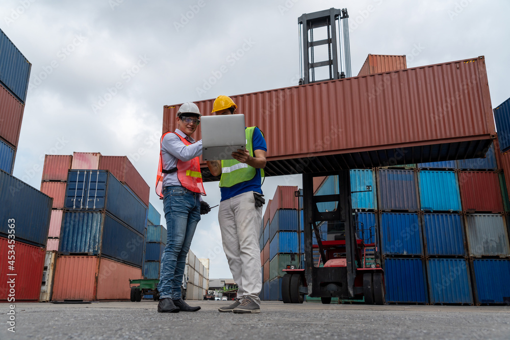 Industrial worker works with co-worker at overseas shipping container yard . Logistics supply chain 