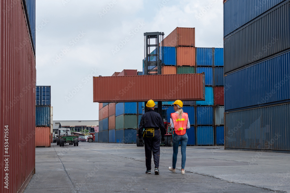 Industrial worker works with co-worker at overseas shipping container yard . Logistics supply chain 