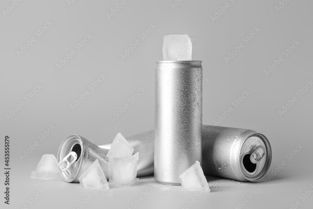 Cans of soda and ice cubes on grey background