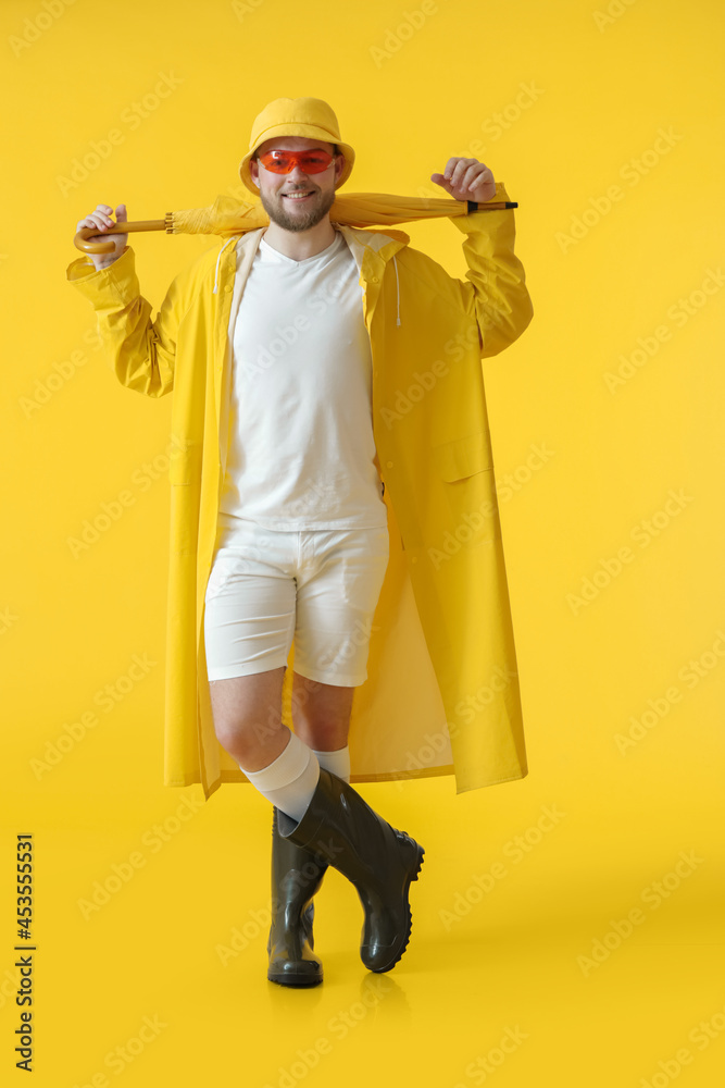 Handsome young man with umbrella on color background