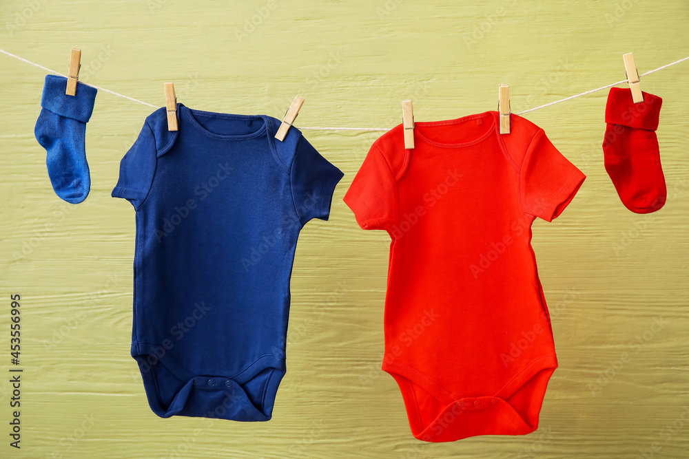 Baby clothes hanging on rope against color wooden background