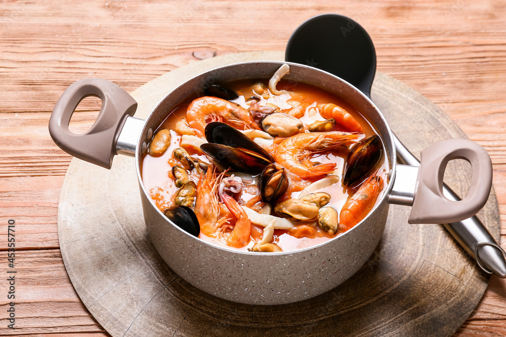 Pot of tasty Cacciucco soup on wooden background