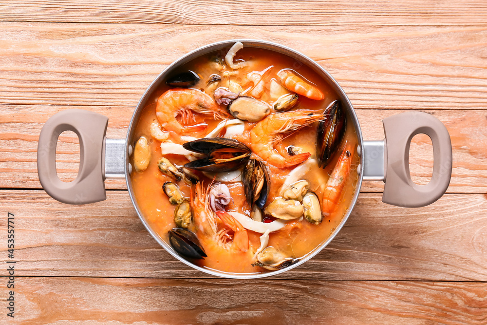 Pot of tasty Cacciucco soup on wooden background