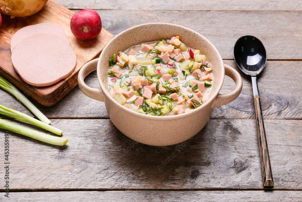 Cooking pot with tasty okroshka and ingredients on wooden background