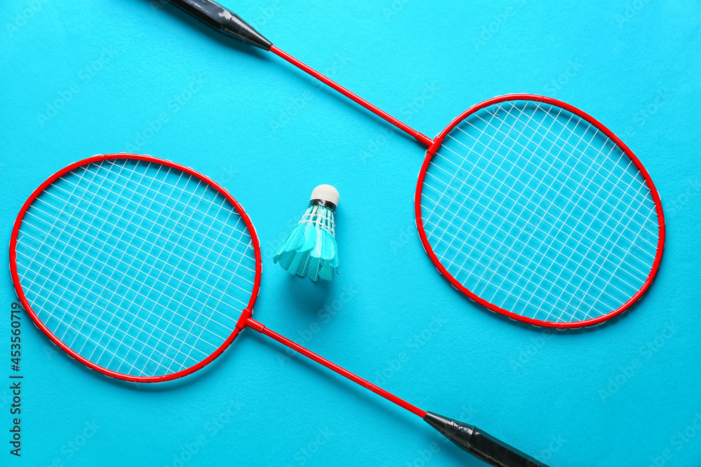 Badminton rackets and shuttlecock on color background