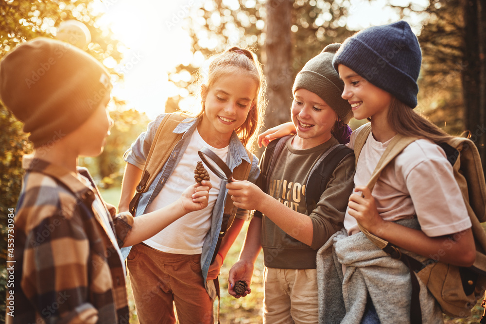 Group of happy school kids in casual clothes with backpacks exploring nature and forest together