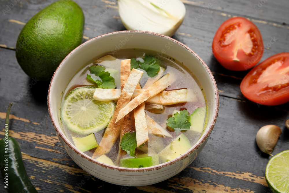 Bowl of tasty Sopa de Lima soup and ingredients on table, closeup