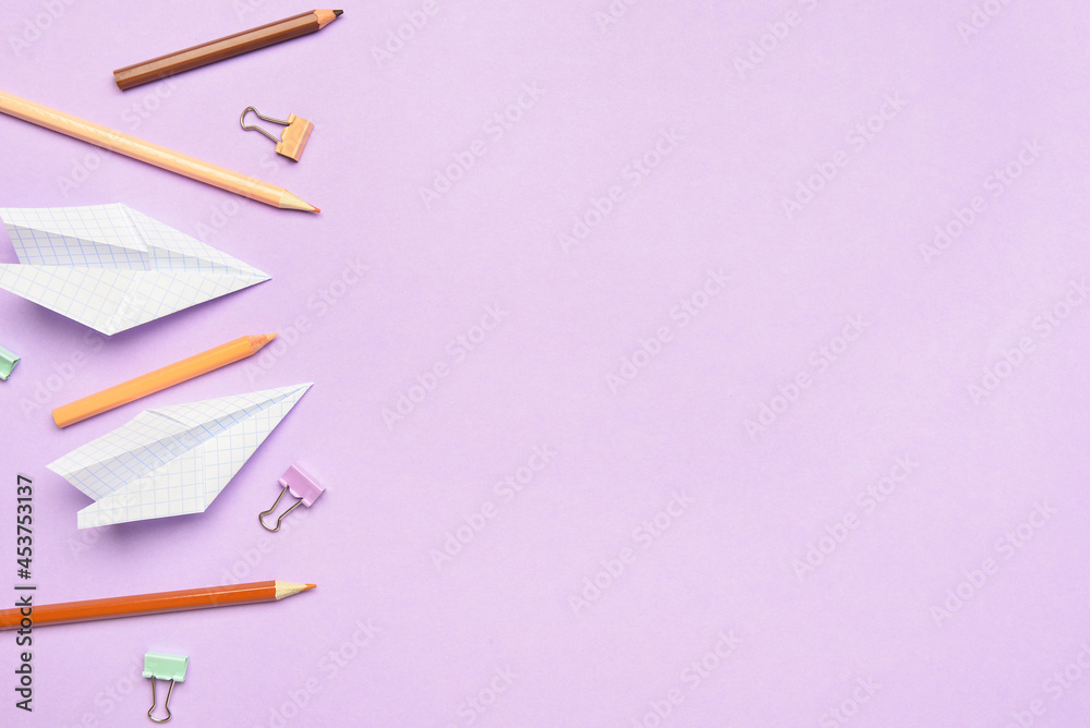 Paper airplanes with pencils and clips on color background