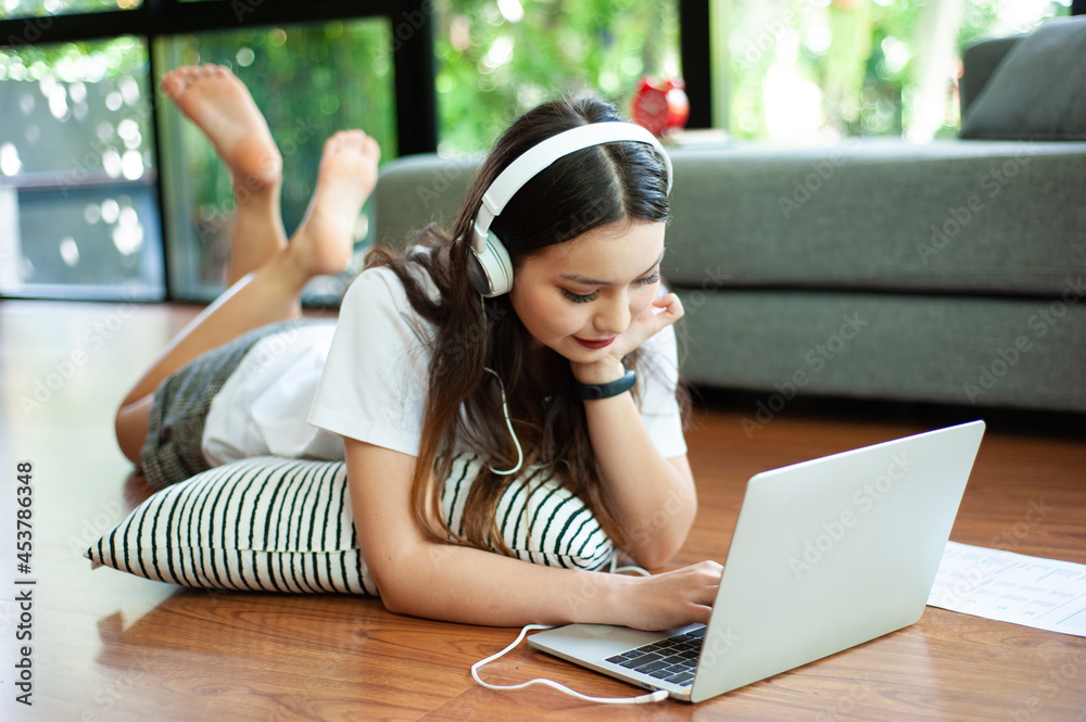 Girl lying on pillow at home watching movies, listening to music from the Internet on laptop.