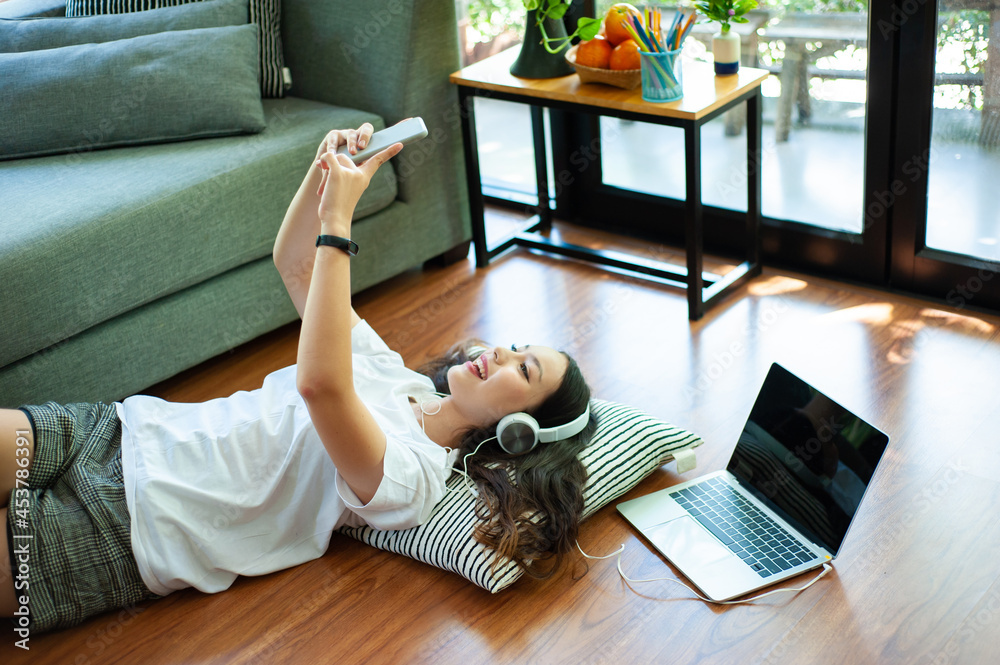 Girl listening to music with headphones playing mobile phone and lying on the floor in the living ro