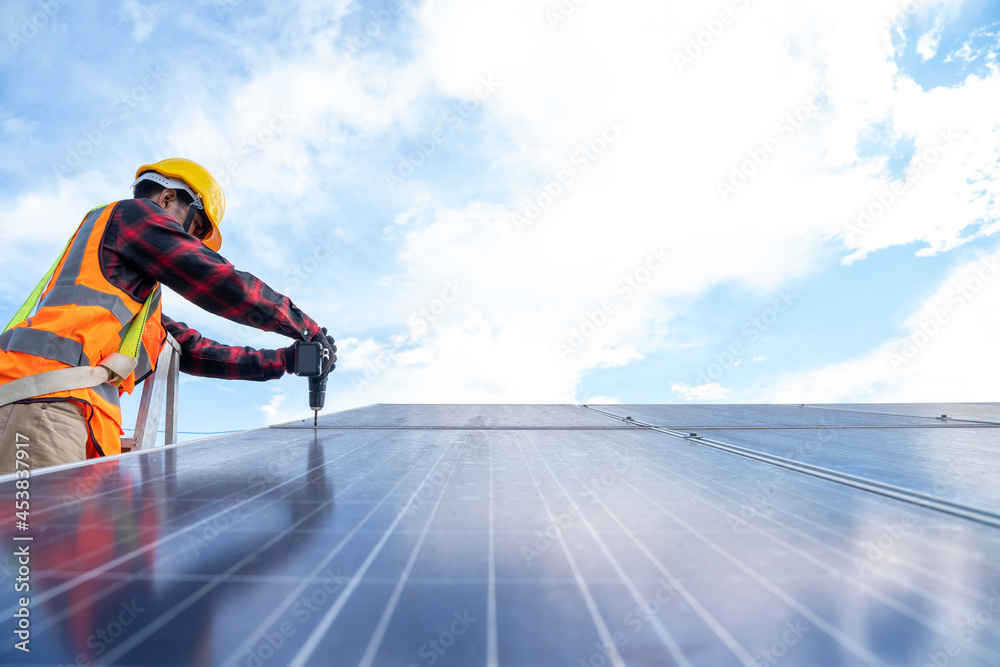 Solar panel technician with drill installing solar panels on roof at solar panel field,Environmental