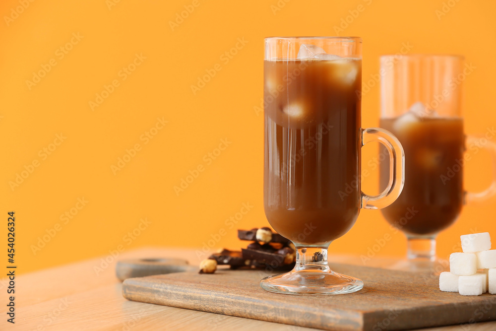 Wooden board with glass cups of tasty iced coffee, sugar cubes and chocolate on table