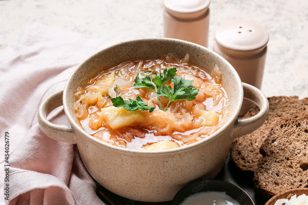 Pot with tasty sauerkraut soup on light background