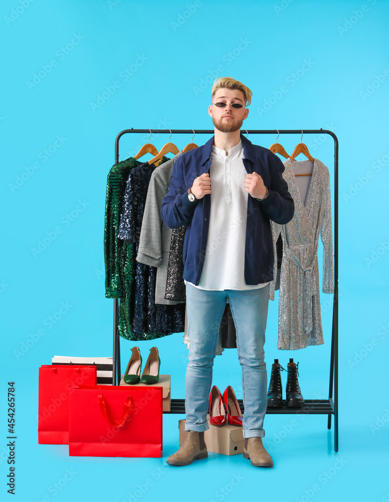 Male stylist near rack with clothes on color background