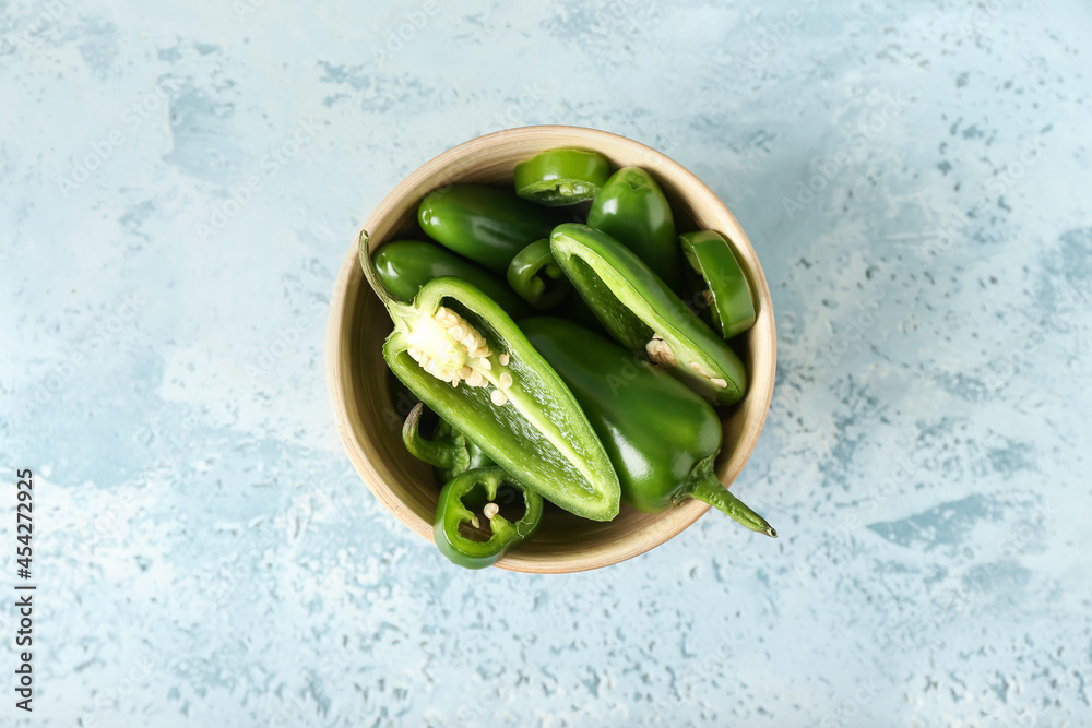 Bowl with cut green jalapeno peppers on color background