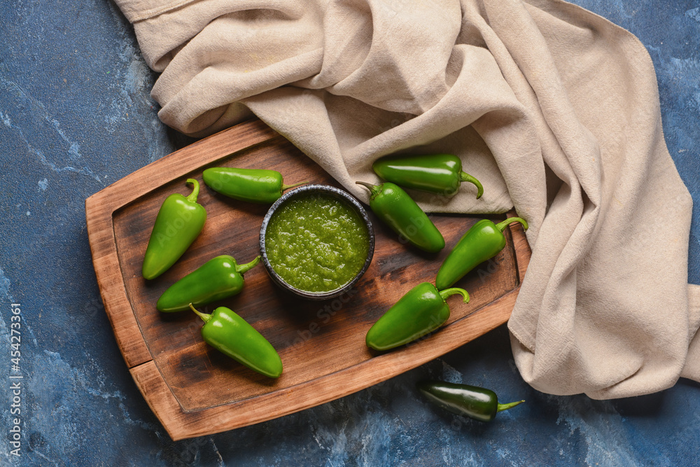 Bowl of Tomatillo Salsa Verde sauce and jalapeno pepper on color background