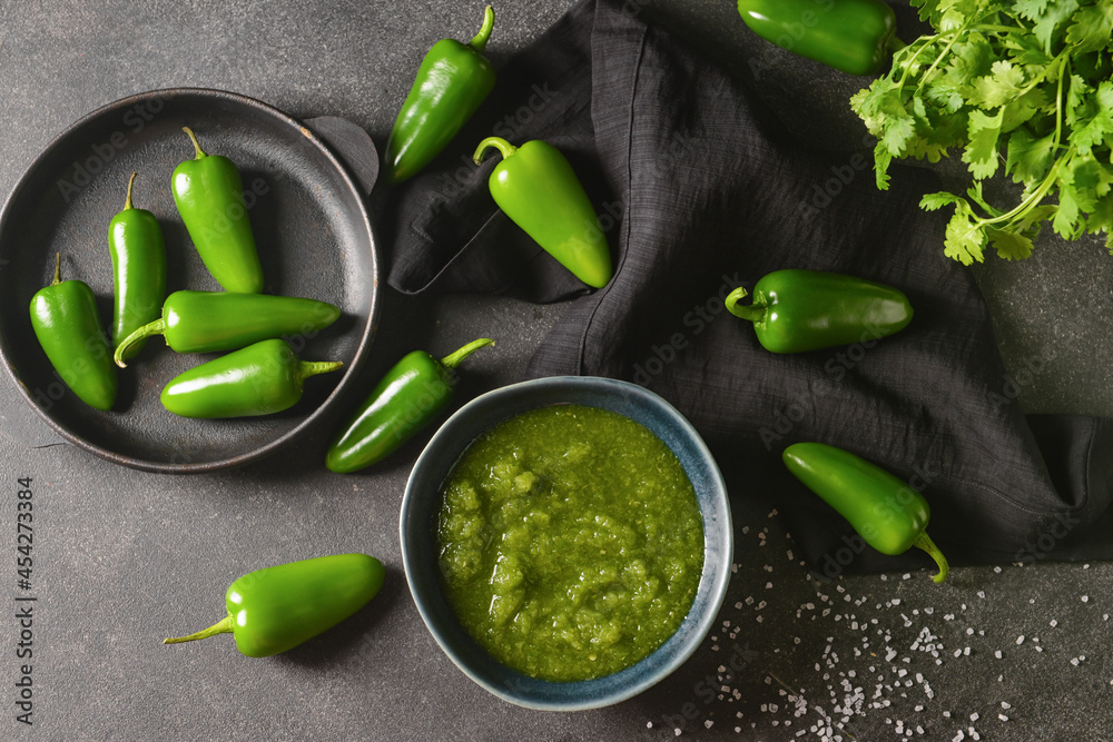 Bowl of Tomatillo Salsa Verde sauce and jalapeno pepper on dark background