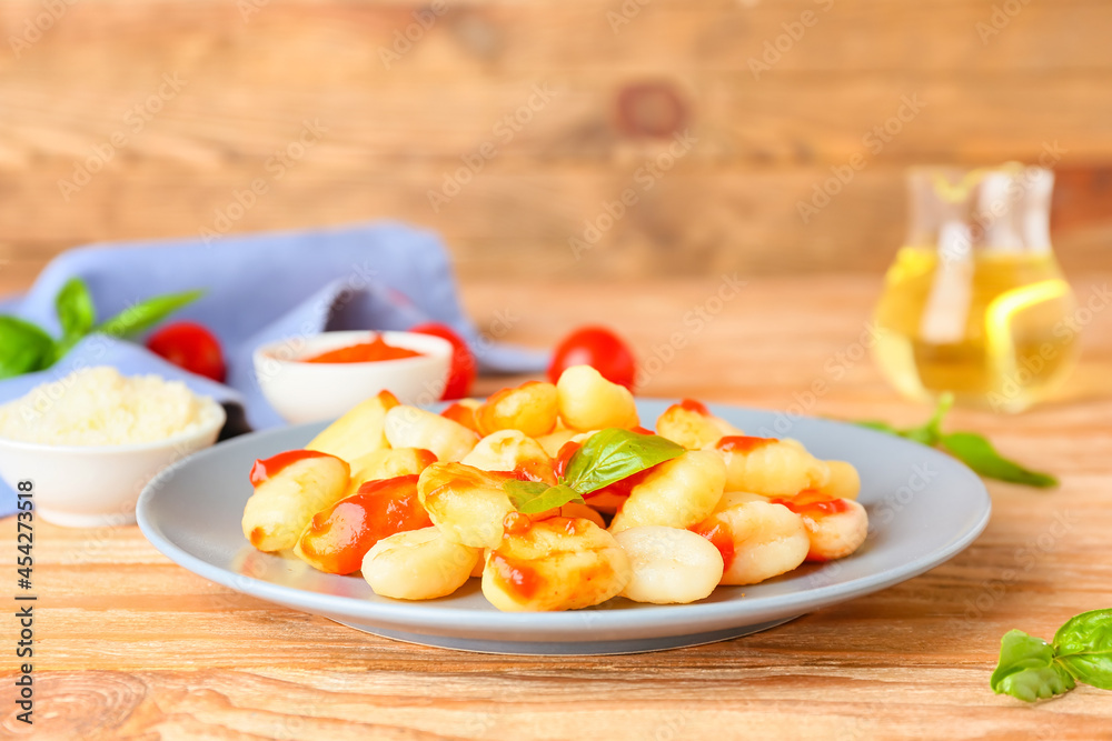 Delicious gnocchi with tomato sauce in plate on wooden table