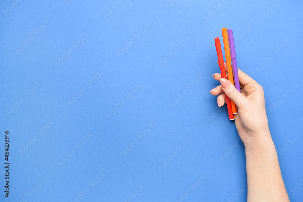 Female hand with colorful markers on color background