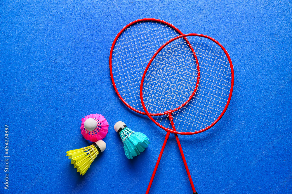 Badminton rackets and shuttlecocks on color background