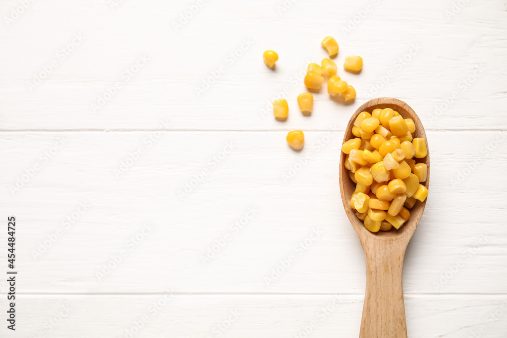 Spoon with corn kernels on light wooden background, closeup