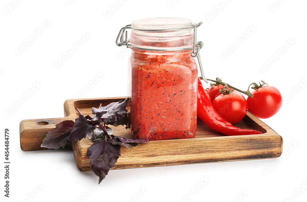 Wooden board with jar of tasty pesto sauce, fresh basil, tomatoes and chili pepper on white backgrou