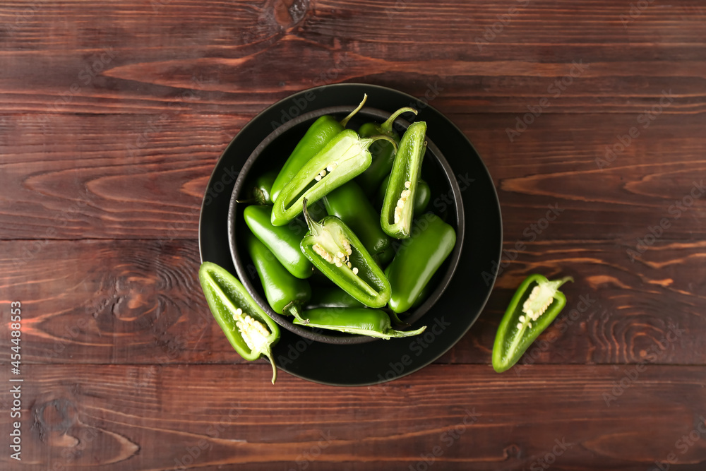 Bowl with cut green jalapeno peppers on wooden background