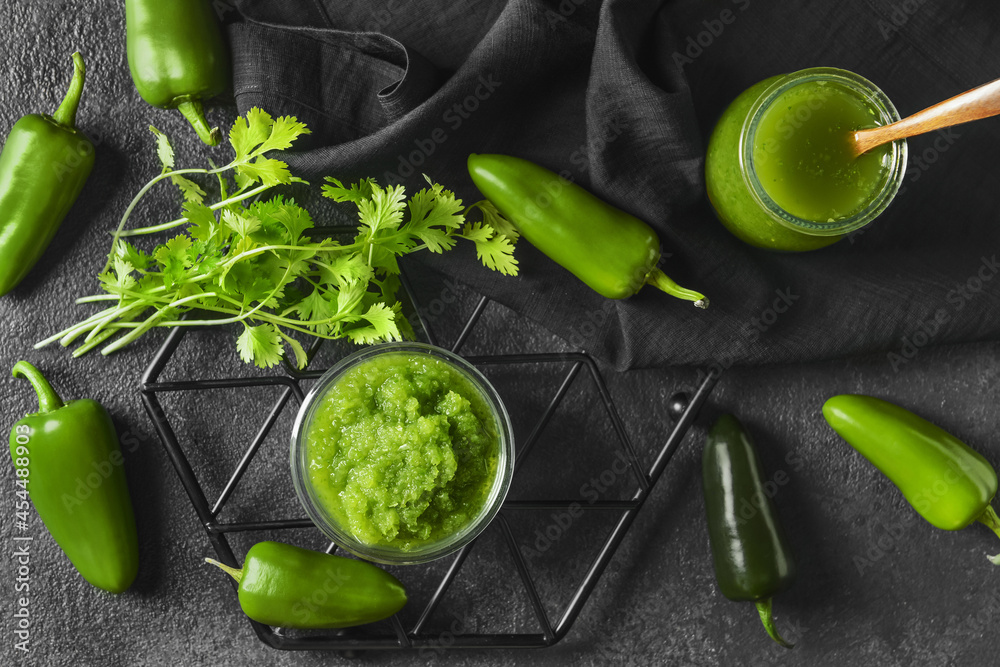 Glass jar and bowl with Tomatillo Salsa Verde sauce and ingredients on dark background