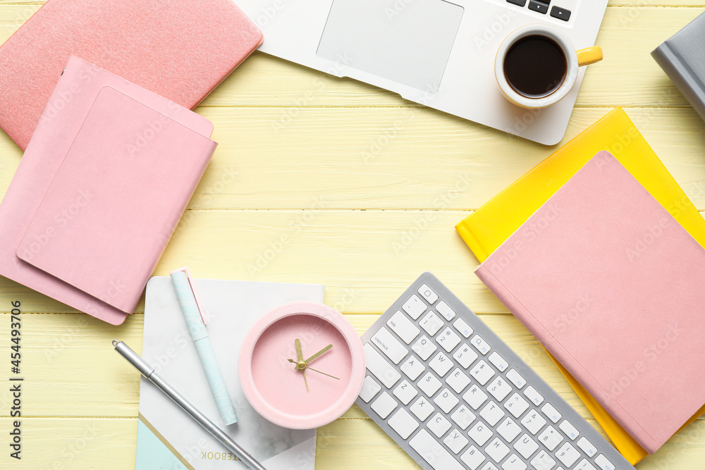 Alarm clock with office supplies, cup of coffee and laptop on color wooden background