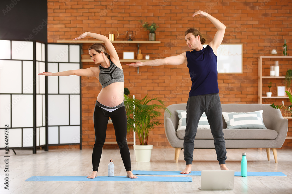 Young pregnant woman and her husband practicing yoga at home