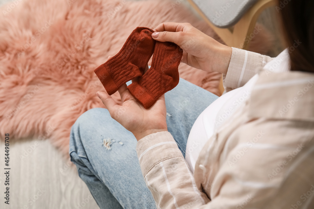 Pregnant woman with baby socks at home, closeup