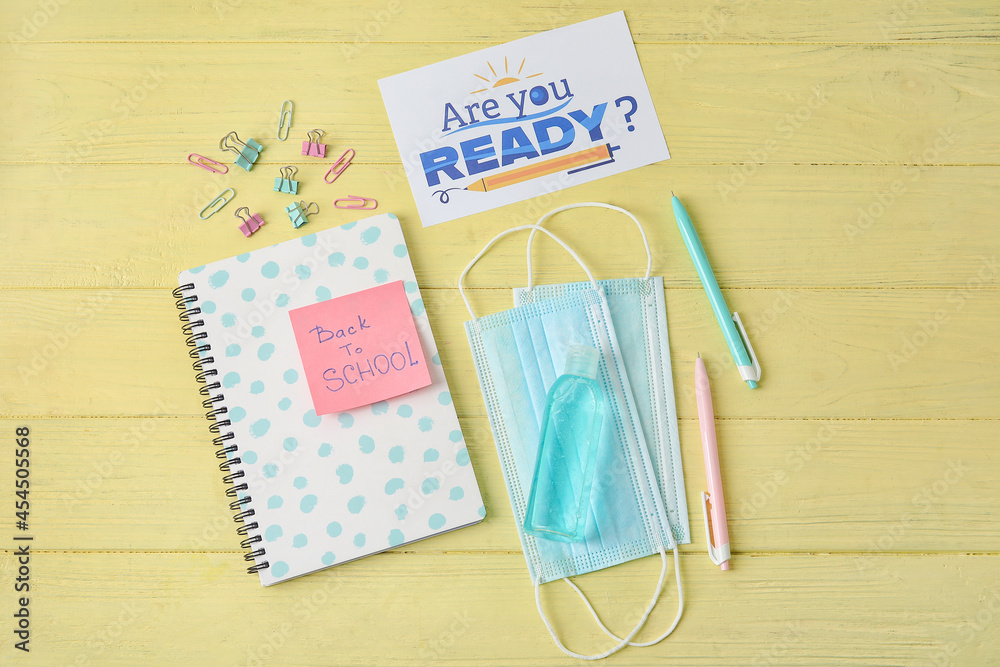 Paper with text BACK TO SCHOOL, stationery and medical masks on color wooden background