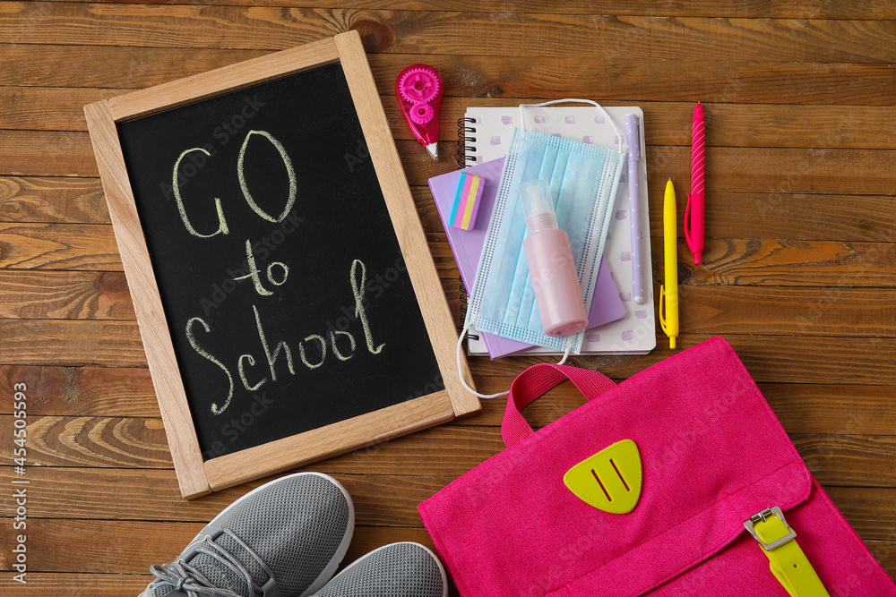 Board with text GO TO SCHOOL, stationery and medical mask on wooden background