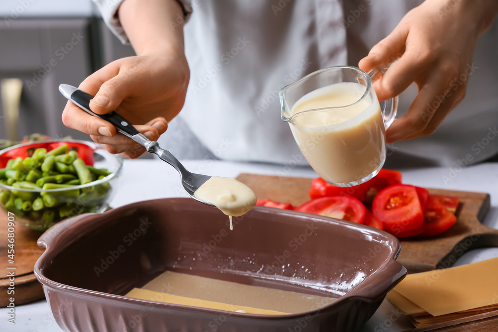 Woman preparing tasty vegetable lasagna at table in kitchen, closeup