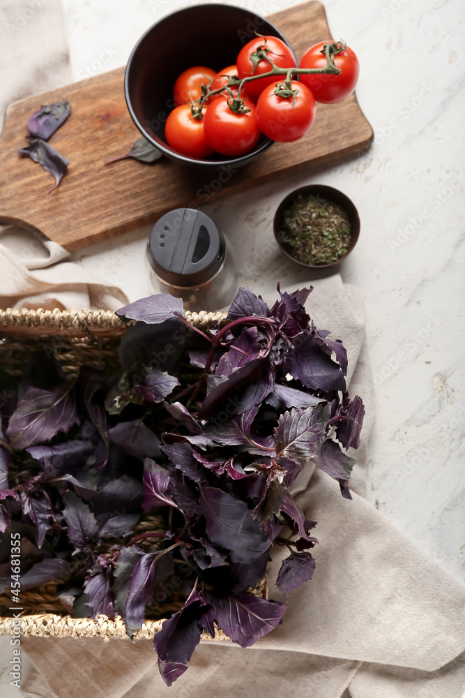 Basket with fresh basil, tomatoes and spices on light background