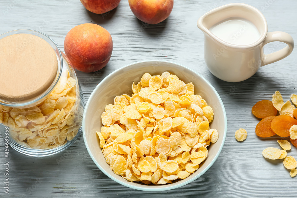 Bowl with tasty cornflakes, fruits and jug of milk on color wooden background