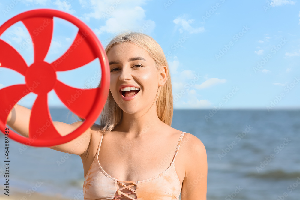 Beautiful young woman with frisbee disk on sea beach