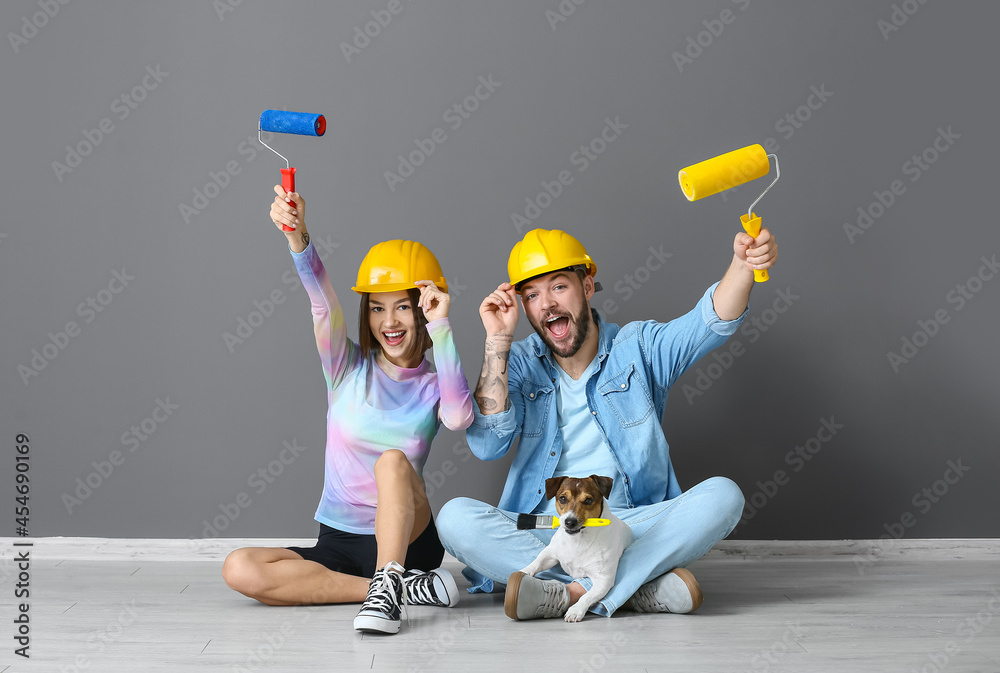 Young couple with painters tools and cute dog near grey wall