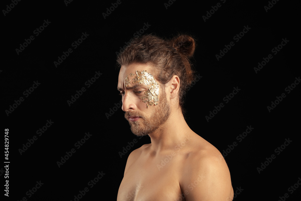 Handsome young man with golden foil on face against black background