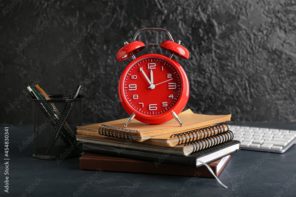 Stylish alarm clock with stationery on dark background