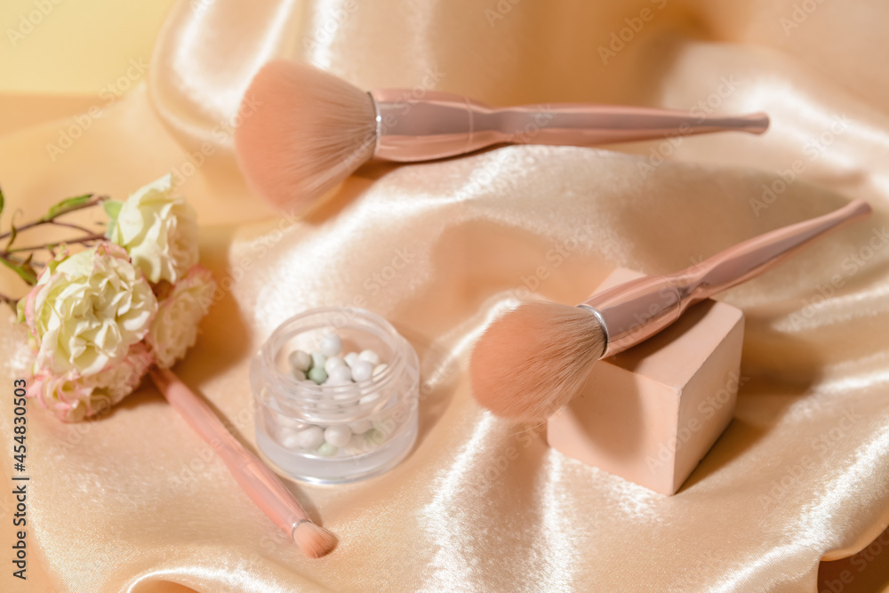 Makeup brushes with powder and decor on fabric background